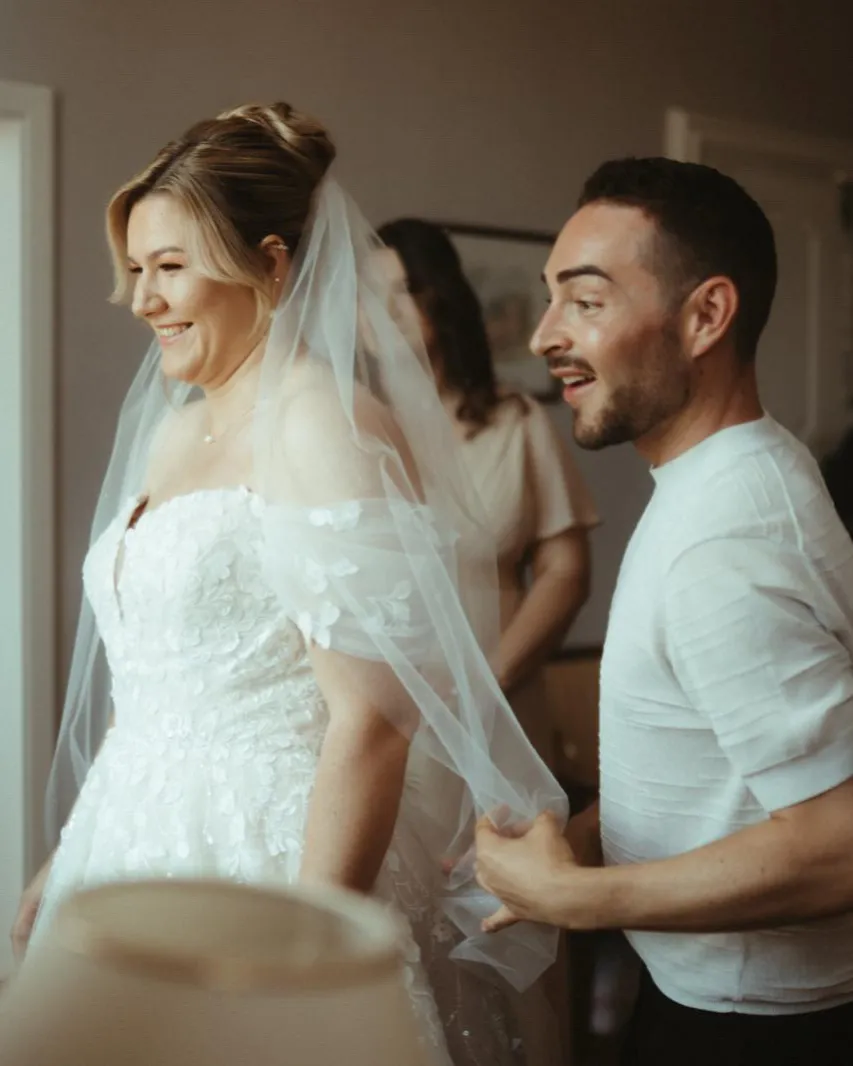 Braut mit Schleier lacht, Micha hilft beim Kleid